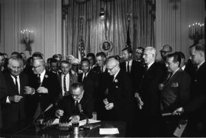 Foto en blanco y negro del presidente Lyndon B. Johnson firmando la Ley de Derechos Civiles de 1964, rodeado de líderes del movimiento por los derechos civiles, incluido Martin Luther King Jr.